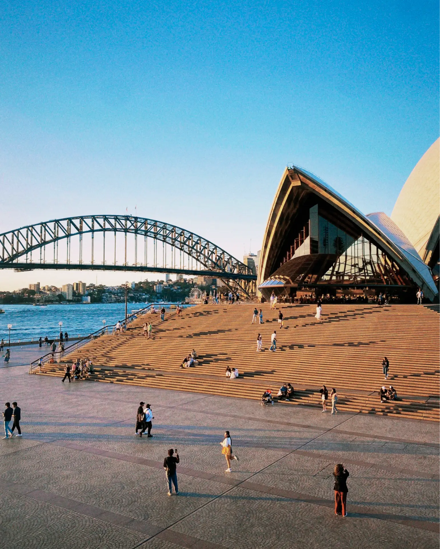 Visitors on the steps of the Sydney Opera House with the Harbour Bridge across the harbour