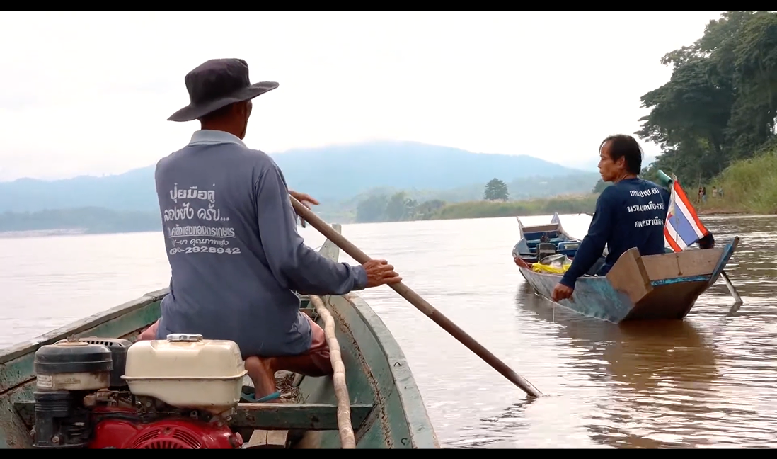 Documentary still — two fishermen paddling wooden boats on the river