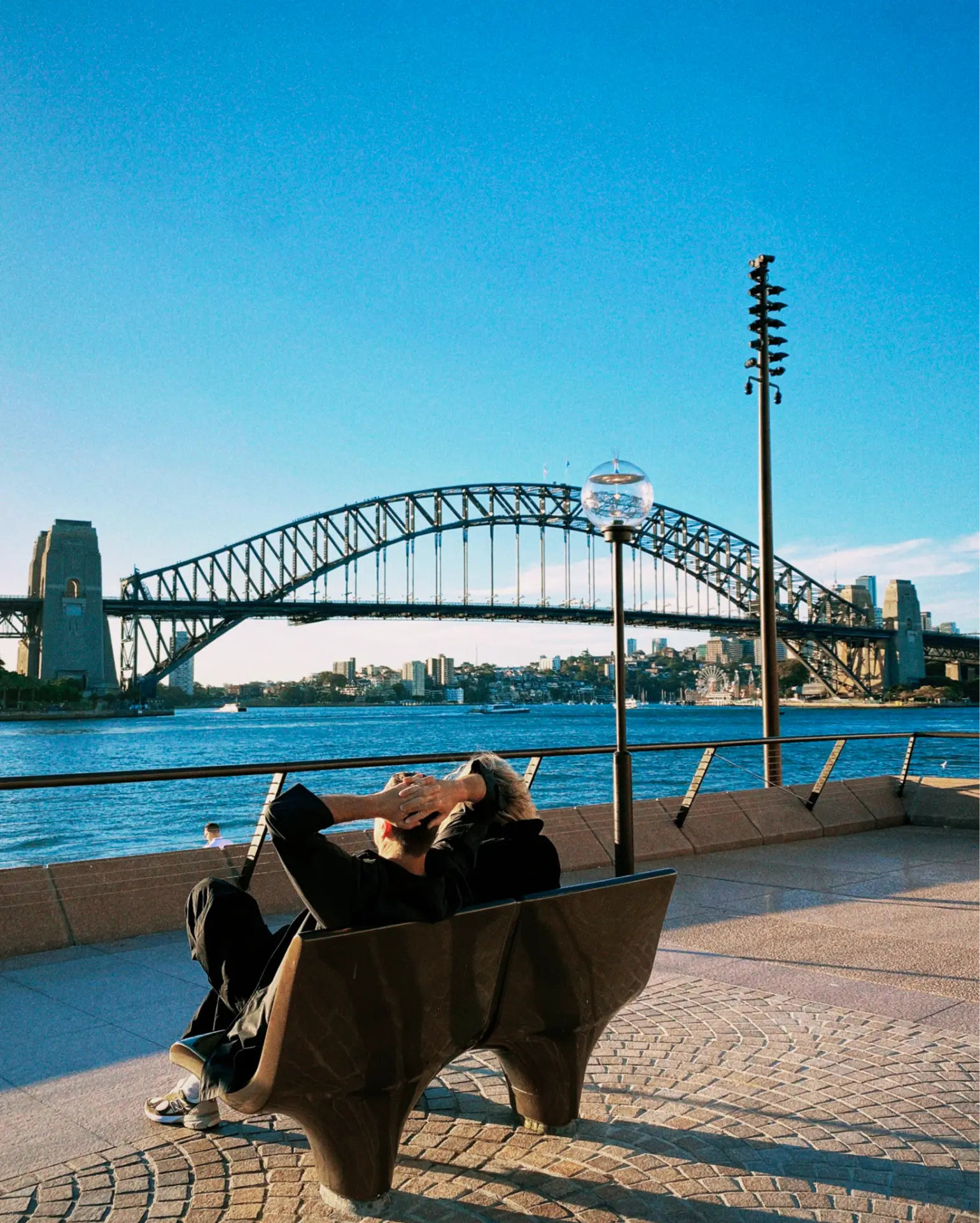 Two people sitting on a bench looking out across the water toward the Sydney Harbour Bridge