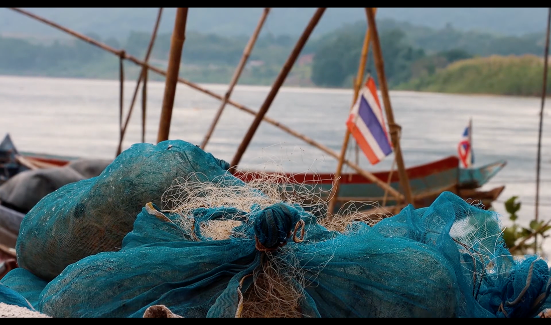 Documentary still — fishing nets and bags by the boats with Thai flags