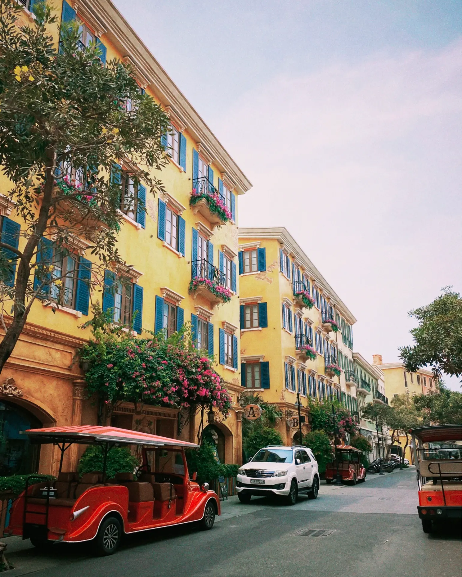 Colourful street with yellow buildings, blue shutters and blooming pink flowers