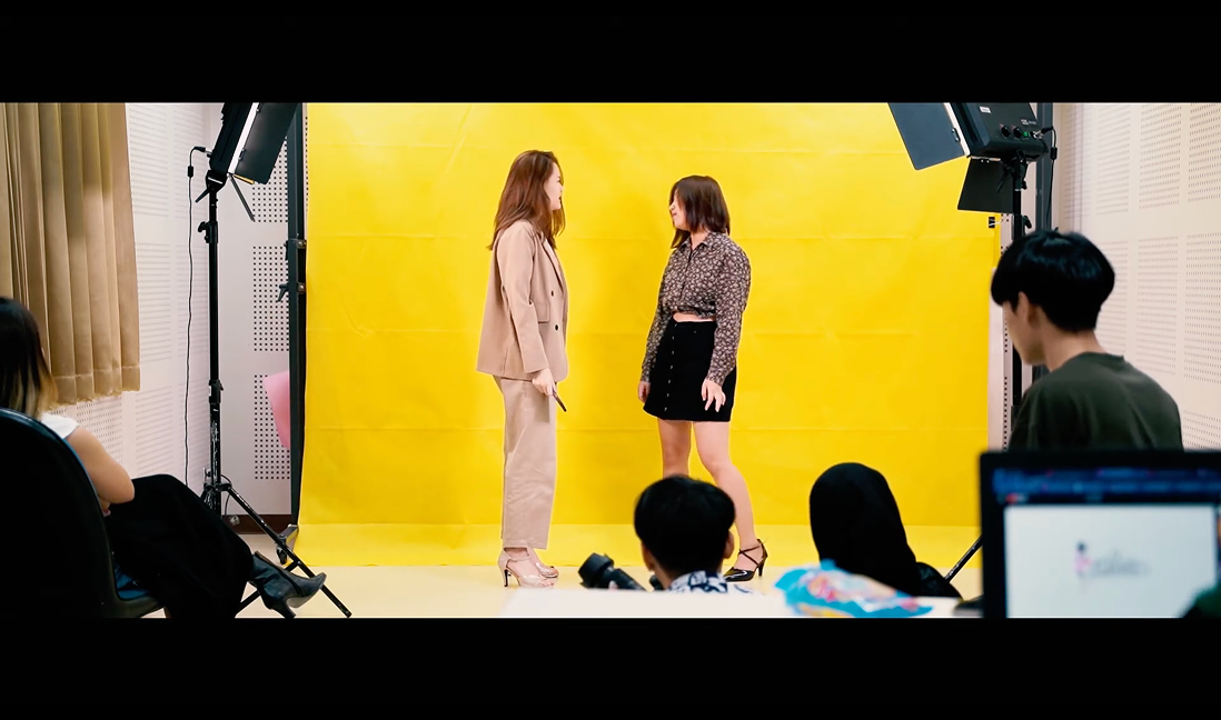 Behind the scenes — two women talking in front of the yellow backdrop