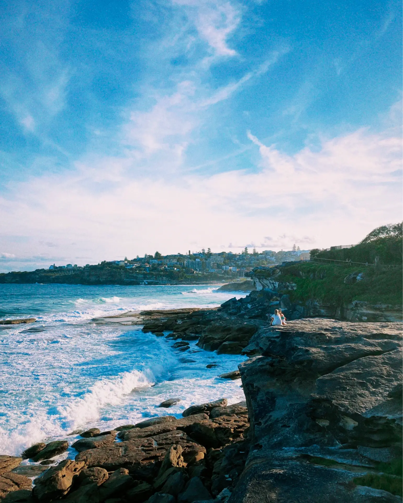 People sitting on coastal cliffs watching waves crash on the rocks