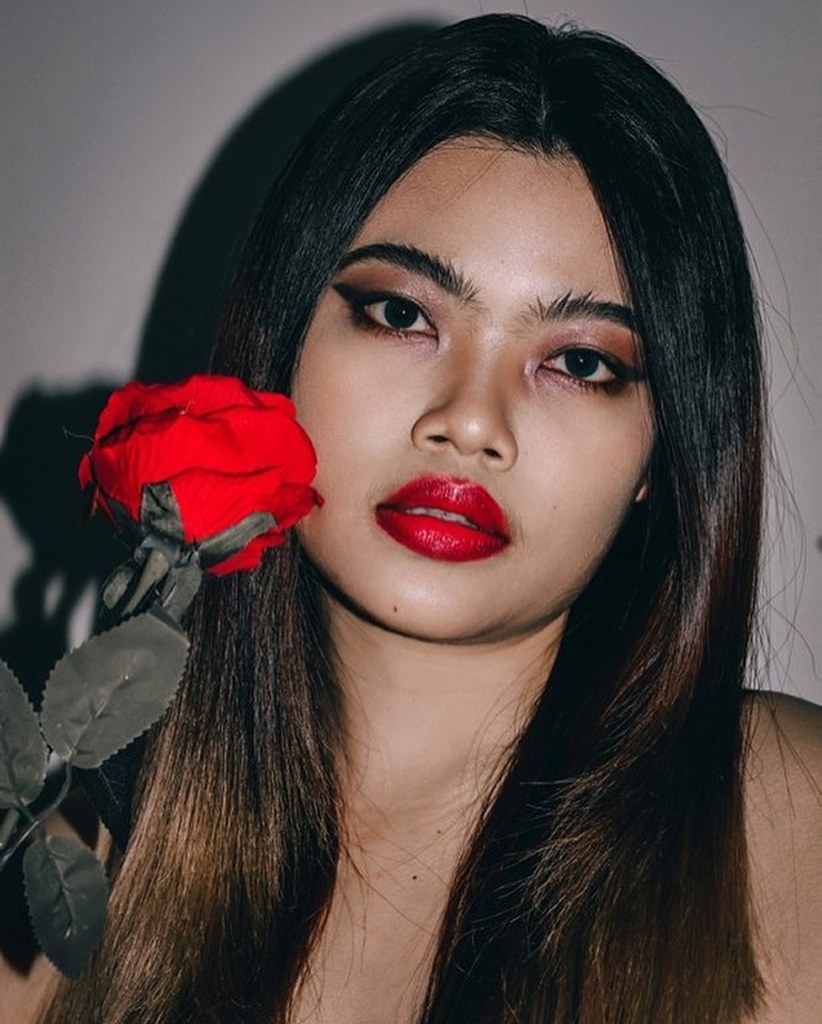 Close-up portrait with a red rose covering one eye