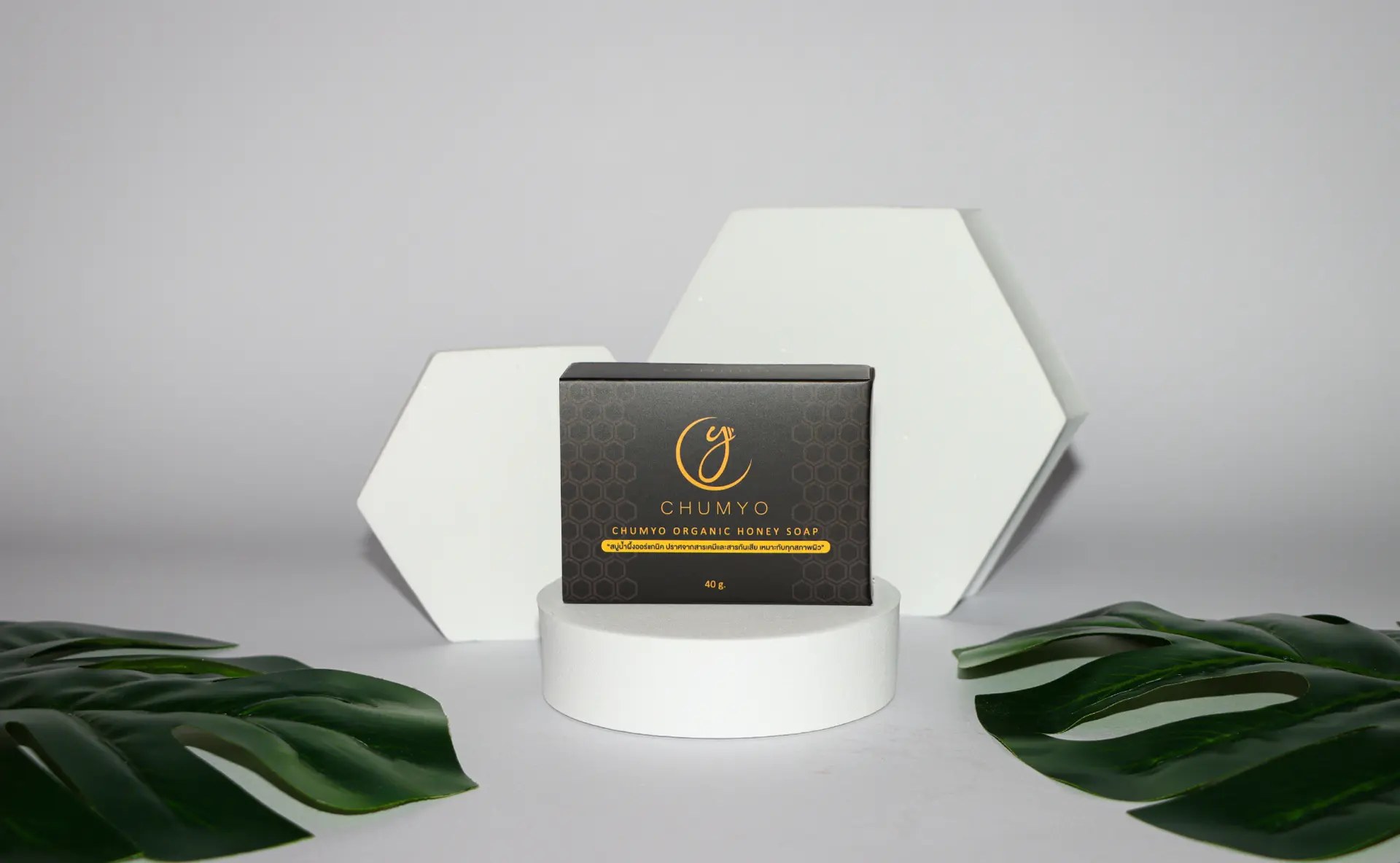 Final product photography of the Chumyo organic honey soap box on a white pedestal with monstera leaves